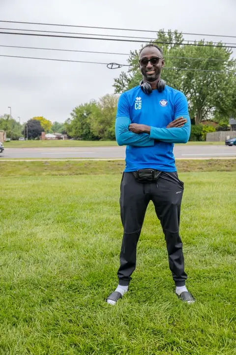 Member in a blue club top standing with arms crossed